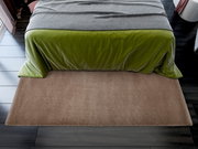 Weiche, beige Matte vor einem Bett mit grünem Überwurf, aus der Vogelperspektive fotografiert.