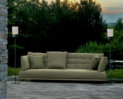 Zwei Akku-Windlichter auf Ständern flankieren ein grünes Sofa im Freien, umgeben von Natur, aus frontaler Perspektive.