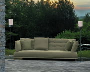 Zwei Akku-Windlichter auf Ständern flankieren ein grünes Sofa im Freien, umgeben von Natur, aus frontaler Perspektive.