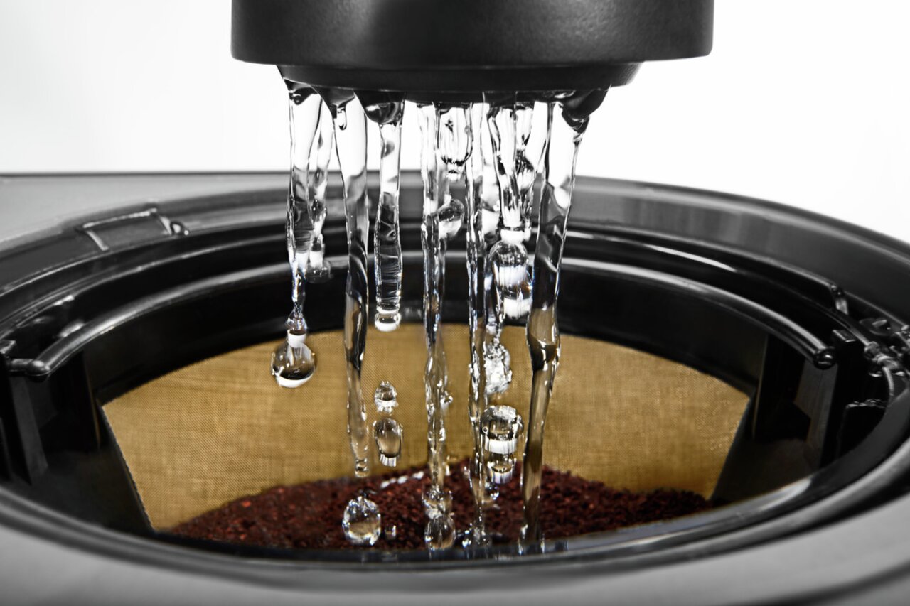 Nahaufnahme des Brühvorgangs einer Kaffeemaschine mit Wasser, das auf Kaffeepulver im Filter tropft.