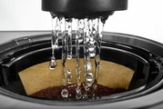 Nahaufnahme des Brühvorgangs einer Kaffeemaschine mit Wasser, das auf Kaffeepulver im Filter tropft.