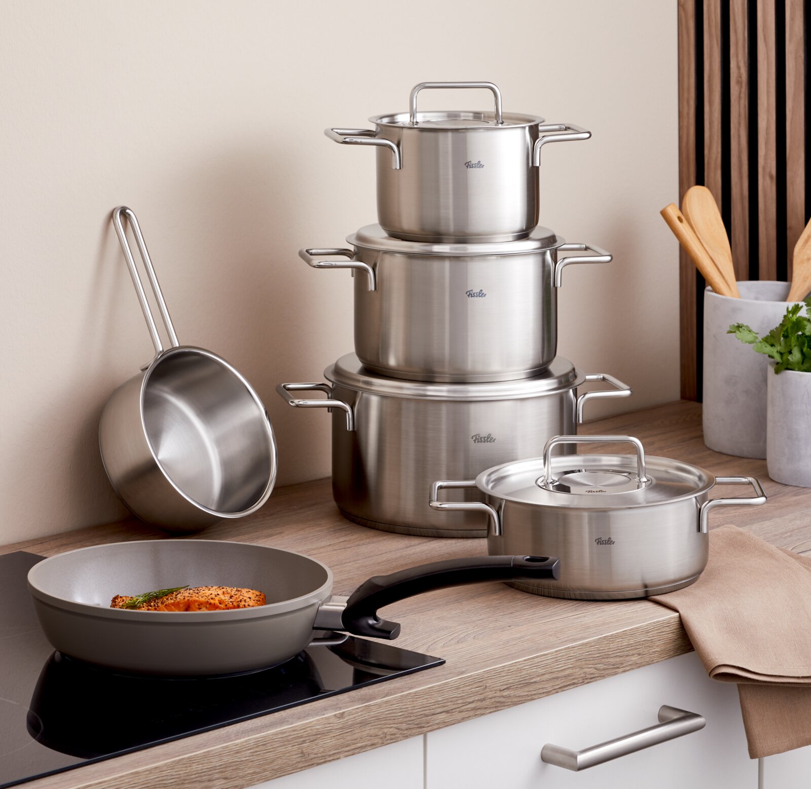 Aanzicht van de keuken met een 5-delige roestvrijstalen pannenset, gestapeld op een aanrechtblad, en een pan met handvat op een fornuis. Vooraanzicht.