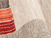Nahaufnahme eines Frisé-Teppichs mit beigen und bunten Streifen in Rot- und Orangetönen, aus seitlicher Perspektive.