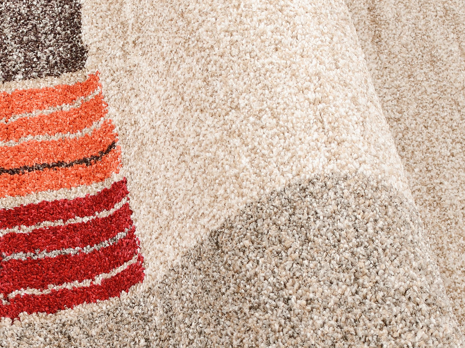 Nahaufnahme eines Frisé-Teppichs mit beigen und bunten Streifen in Rot- und Orangetönen, aus seitlicher Perspektive.