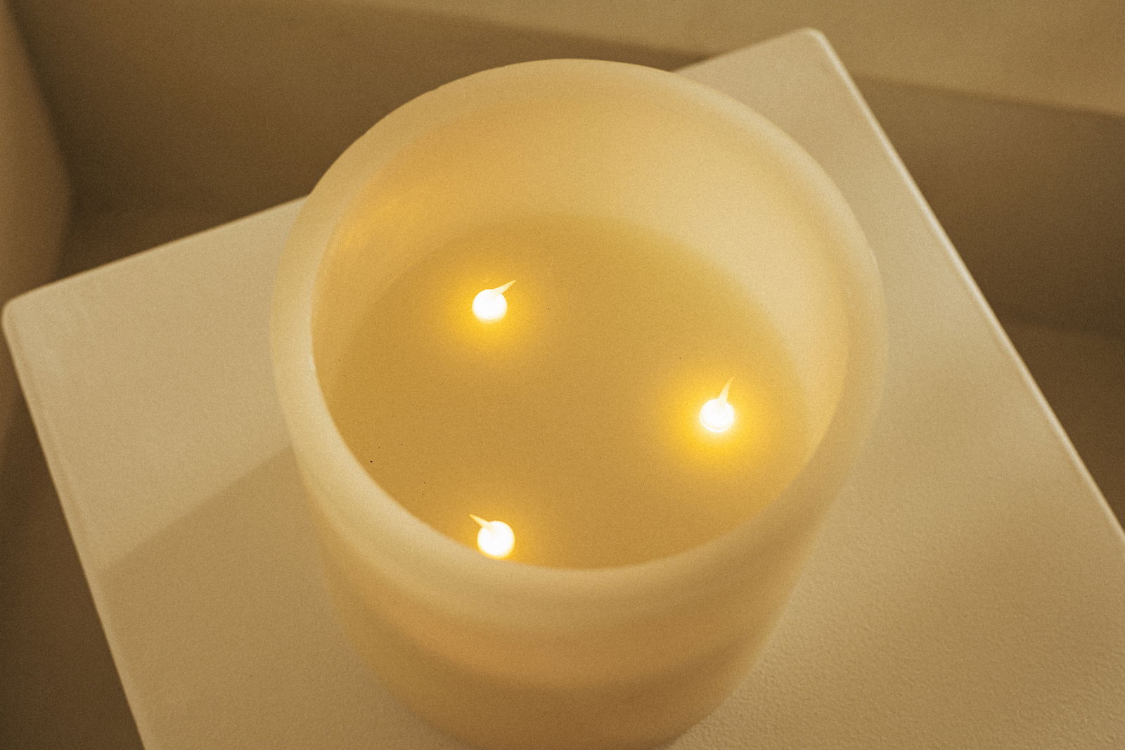 Blick von oben auf eine brennende Outdoor-Kerze mit drei Flammen auf einem weißen Untergrund.