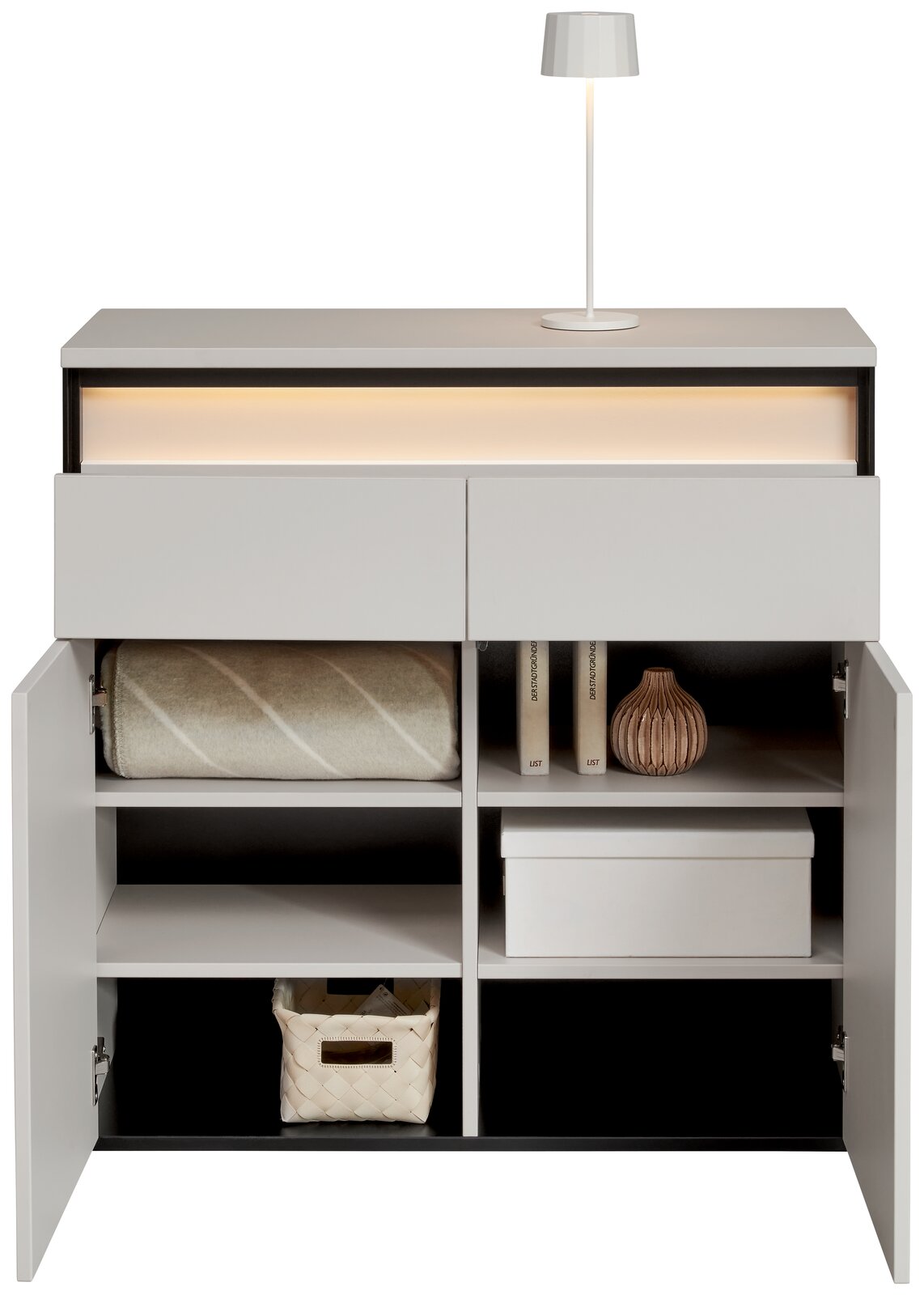 Moderne Kommode mit zwei Schubladen und offenen Türen, die verschiedene Gegenstände wie eine Decke, Bücher, eine Vase und eine Box zeigt. Frontalansicht.