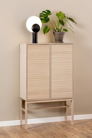 Hochschrank aus hellem Holz mit zwei Türen, darauf eine moderne Lampe und eine grüne Pflanze, seitliche Perspektive