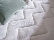 Nahaufnahme einer weißen Matratze mit geprägtem Muster und einem grünen Kissen, von oben fotografiert.