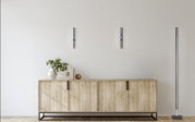 Moderne LED-Stehleuchte BEN in einem eleganten, minimalistischen Design, stehend neben einem Holzschrank in einem hellen Raum. Die Perspektive zeigt die Leuchte von vorne.