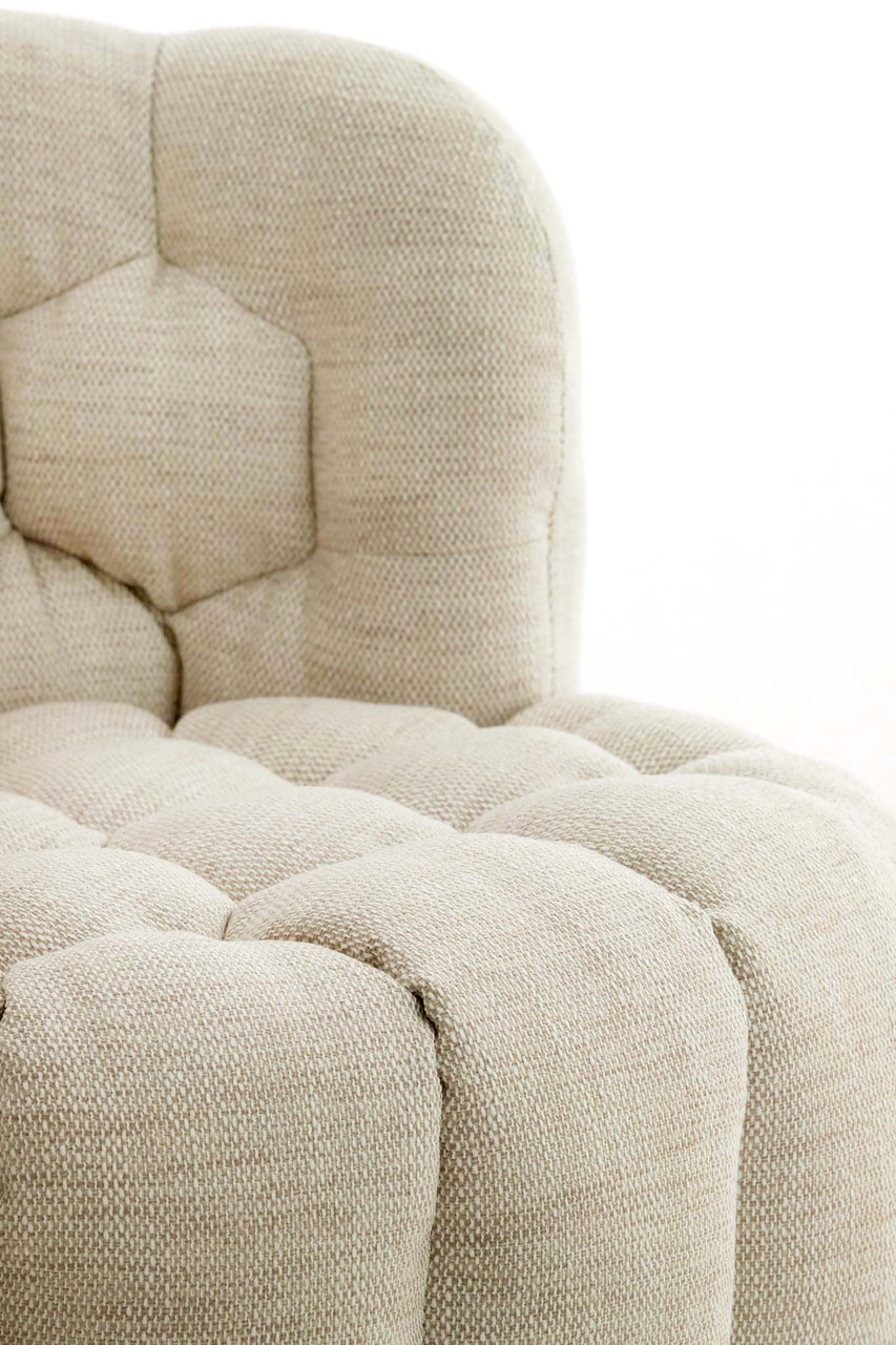 Nahaufnahme eines beigen Sessels mit gepolstertem Stoff und Steppmuster, seitliche Perspektive.