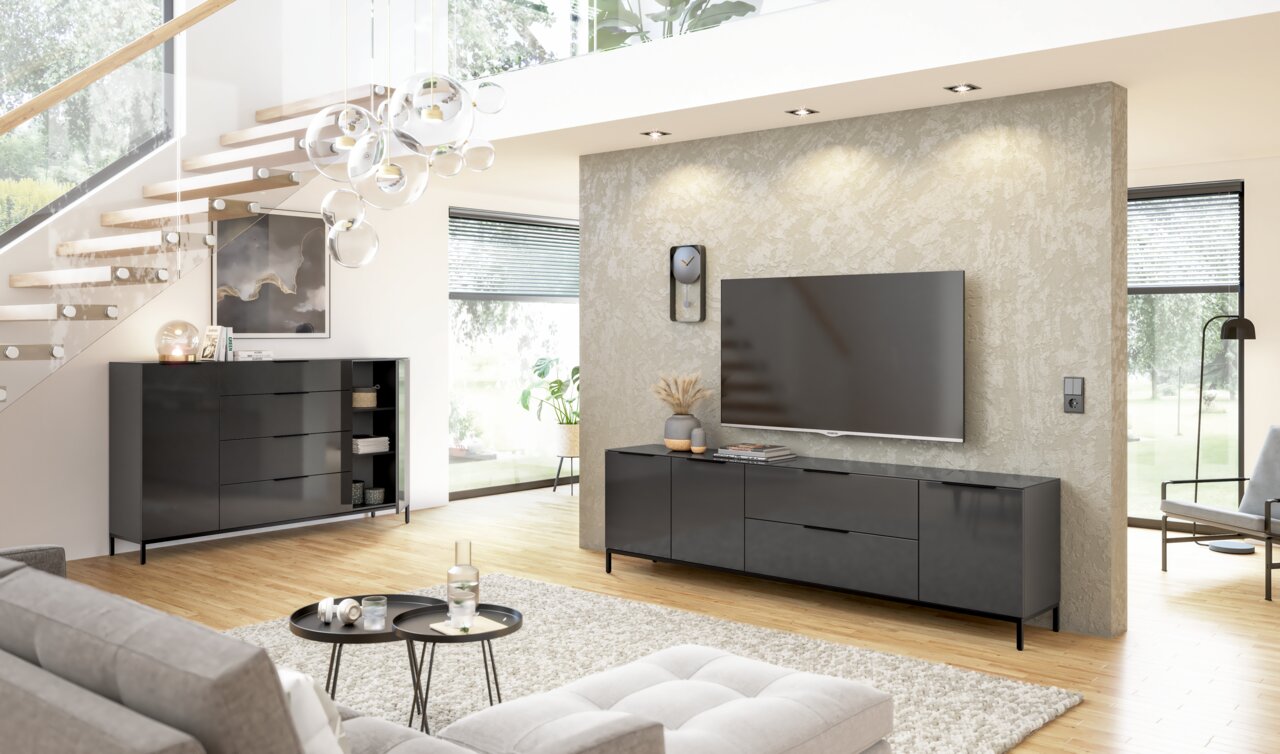 Modernes Wohnzimmer mit einem eleganten, schwarzen Sideboard und einem großen Fernseher an der Wand. Perspektive von vorne auf das Sideboard.