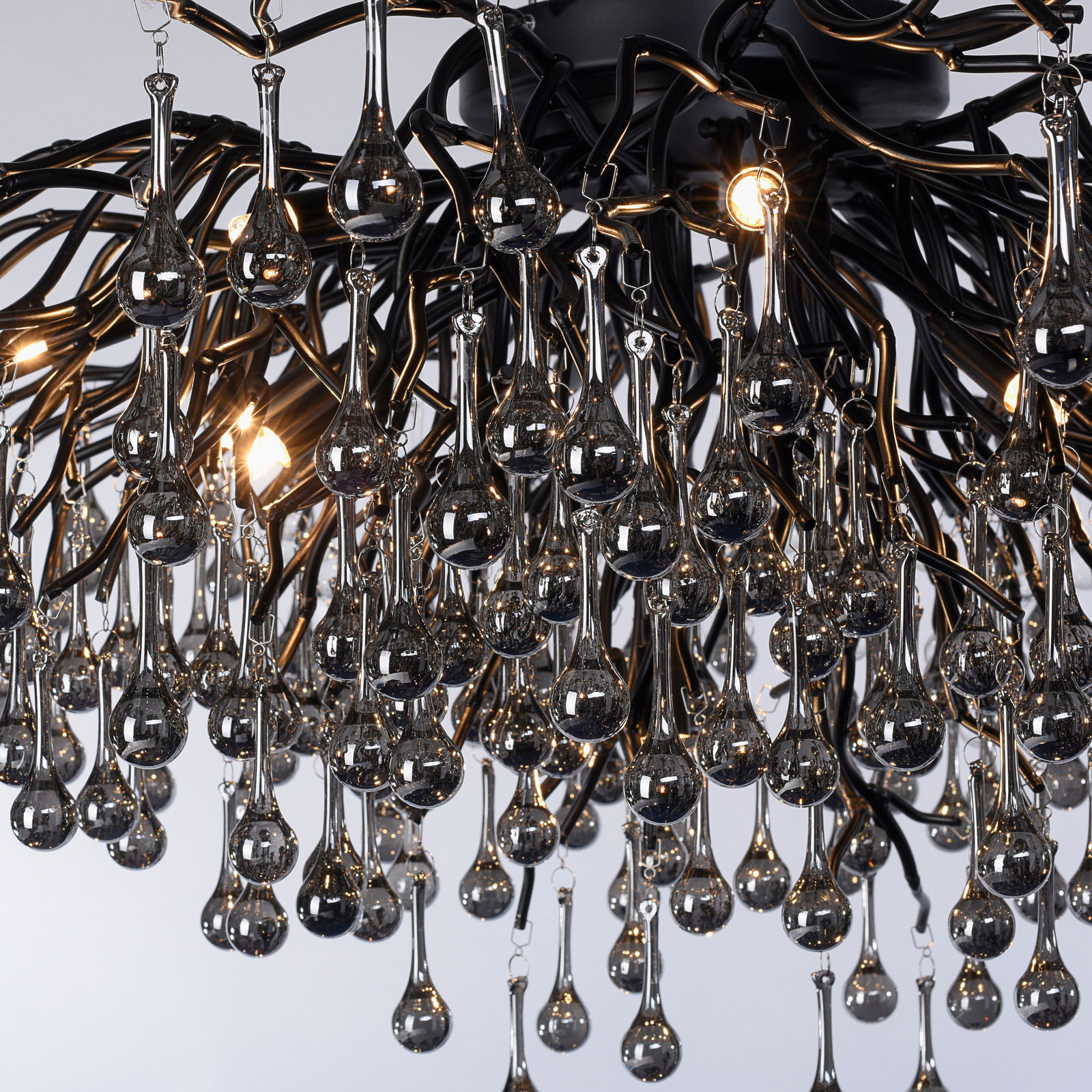 Nahaufnahme einer Deckenleuchte mit tropfenförmigen Glaselementen und schwarzem Metallgestell, von unten betrachtet.