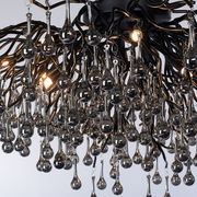 Nahaufnahme einer Deckenleuchte mit tropfenförmigen Glaselementen und schwarzem Metallgestell, von unten betrachtet.