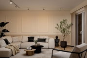 Modernes Wohnzimmer mit beigem Ecksofa, schwarzen und holzfarbenen Couchtischen, dekorativen Vasen und großen Zimmerpflanzen neben Fensterfront; Perspektive: frontale Weitwinkelaufnahme auf Augenhöhe.