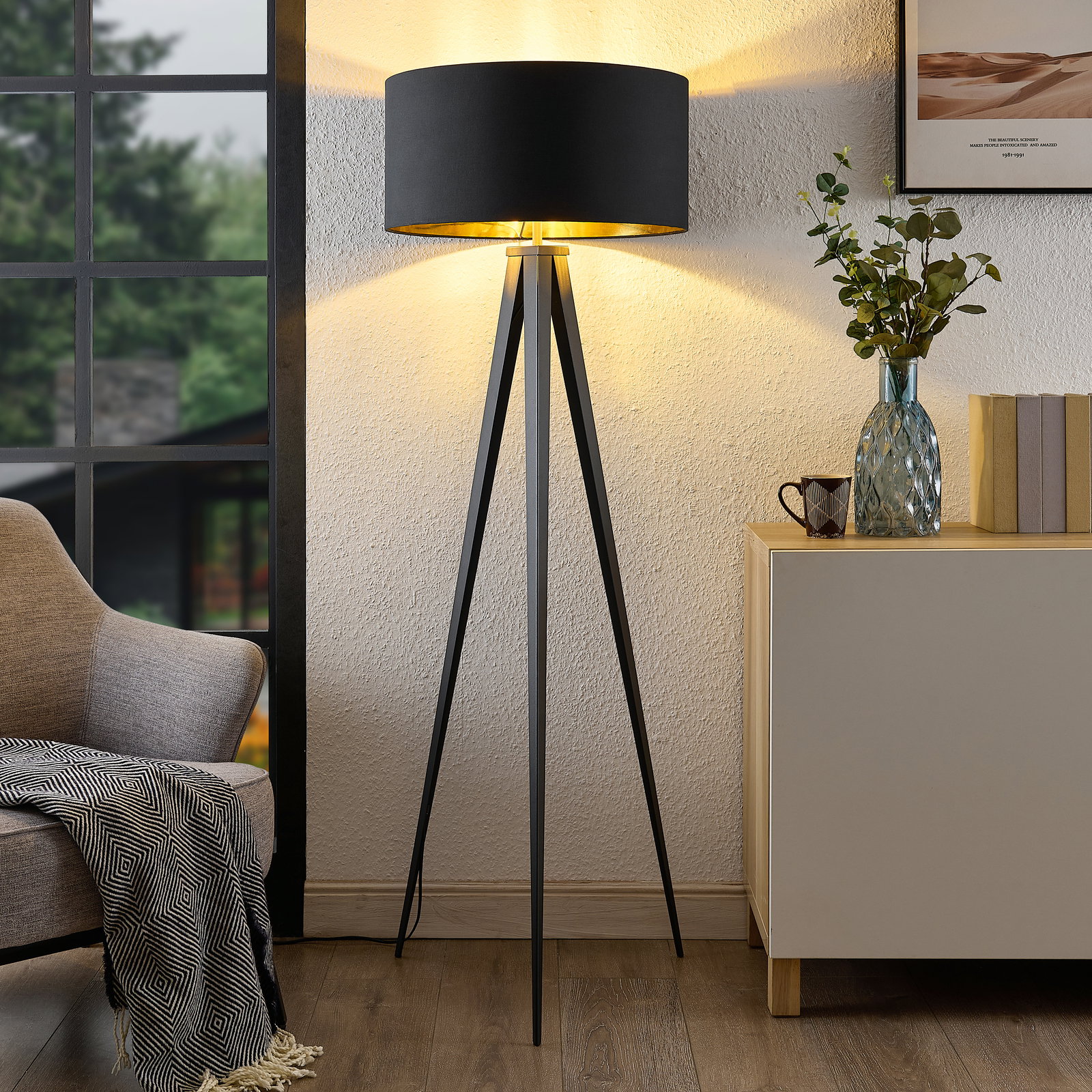 Moderne Stehleuchte mit schwarzem Schirm und dreibeinigem Stativ, seitliche Perspektive im Wohnzimmer.