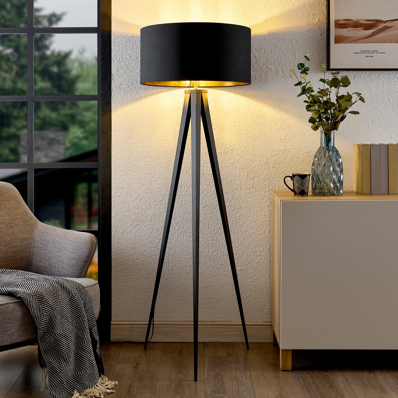 Moderne Stehleuchte mit schwarzem Schirm und dreibeinigem Stativ, seitliche Perspektive im Wohnzimmer.