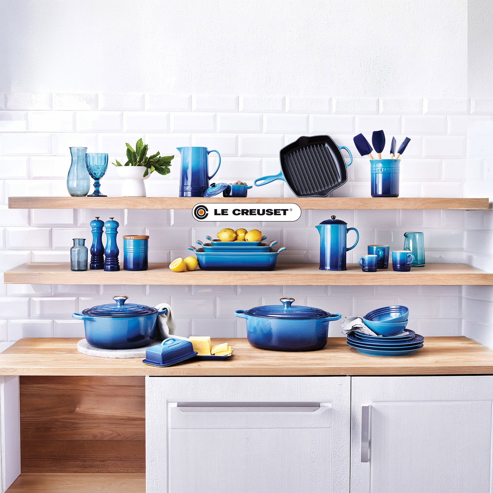 Le Creuset Küchenserie in Blau stilvoll auf offenen Holzregalen präsentiert