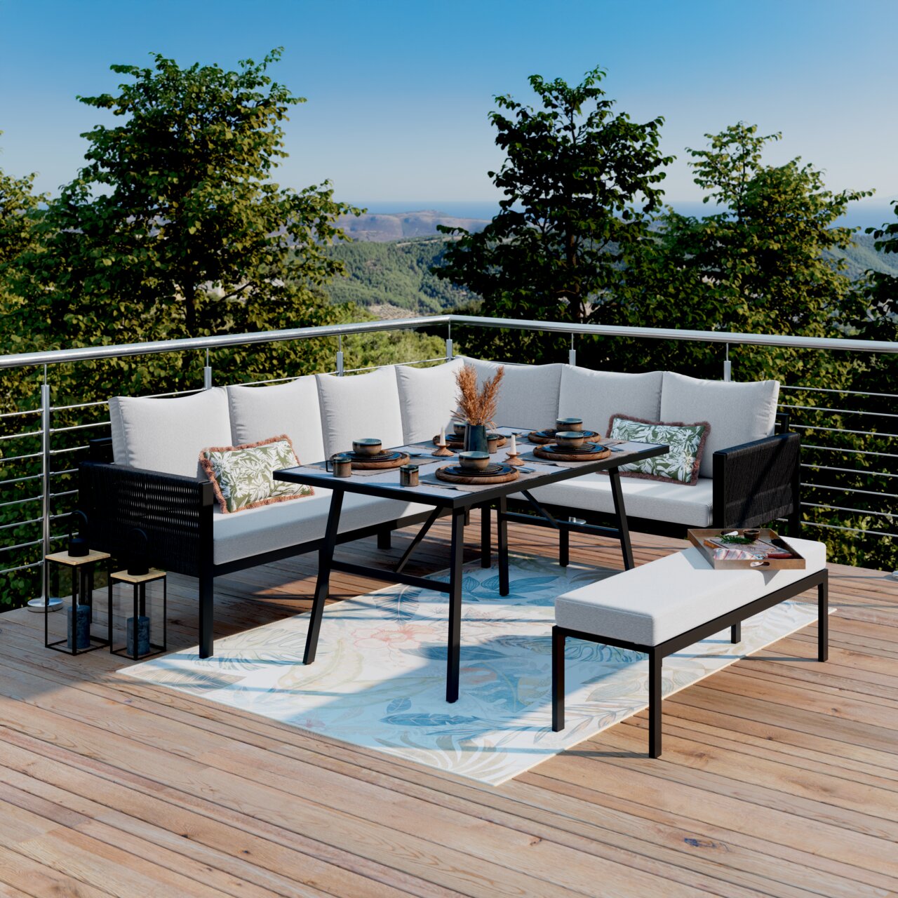 Ambia Garden Gartenlounge-Set MARIKA Moderne Outdoor-Lounge-Essgruppe auf Holzterrasse: L-förmiges Sofa mit hellen Polstern, schwarzer Esstisch und Bank auf gemustertem Teppich, mit gedecktem Tisch und Bergblick im Hintergrund, Perspektive frontal leicht erhöht.