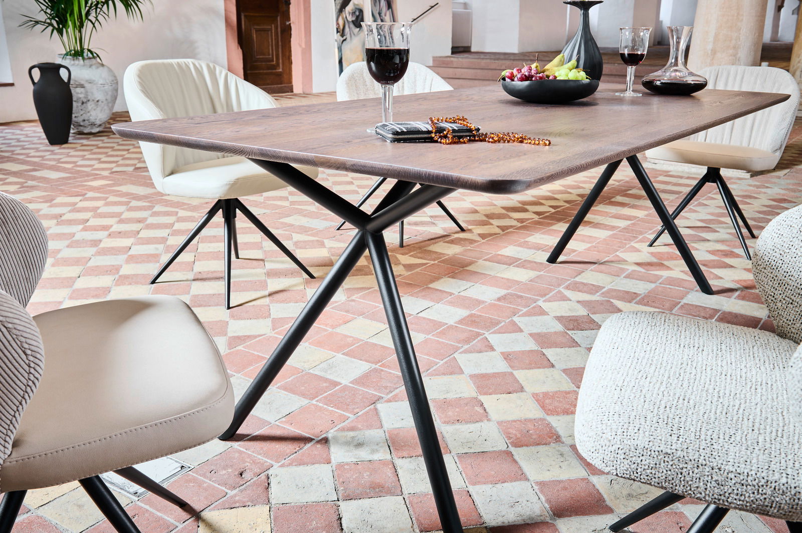 Moderner Esstisch aus Holz mit schwarzem Metallgestell, umgeben von stilvollen Stühlen in einem eleganten Raum mit Fliesenboden, seitliche Perspektive.