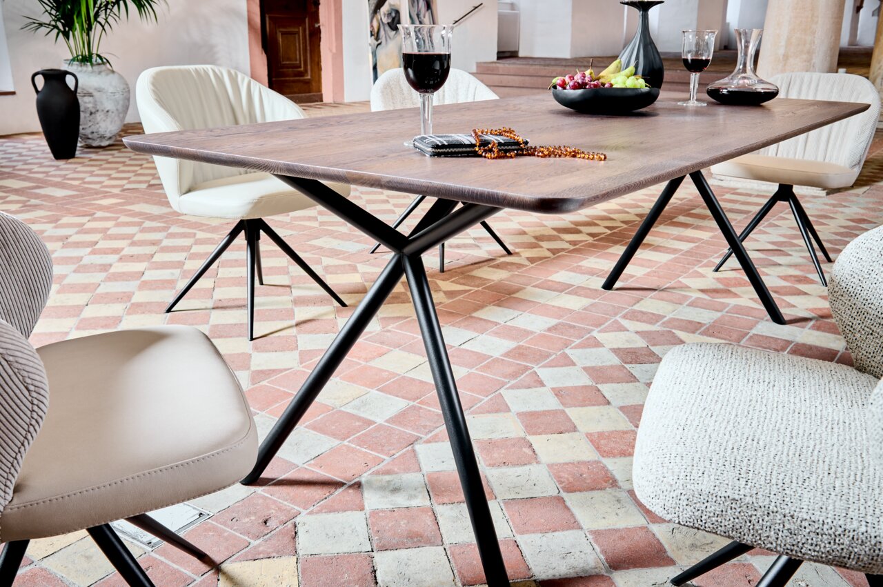 Moderner Esstisch aus Holz mit schwarzem Metallgestell, umgeben von stilvollen Stühlen in einem eleganten Raum mit Fliesenboden, seitliche Perspektive.