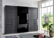 Moderner, dreitüriger Schwebetürenschrank in dunklem Design, frontal abgebildet in einem hellen Raum mit großen Fenstern.