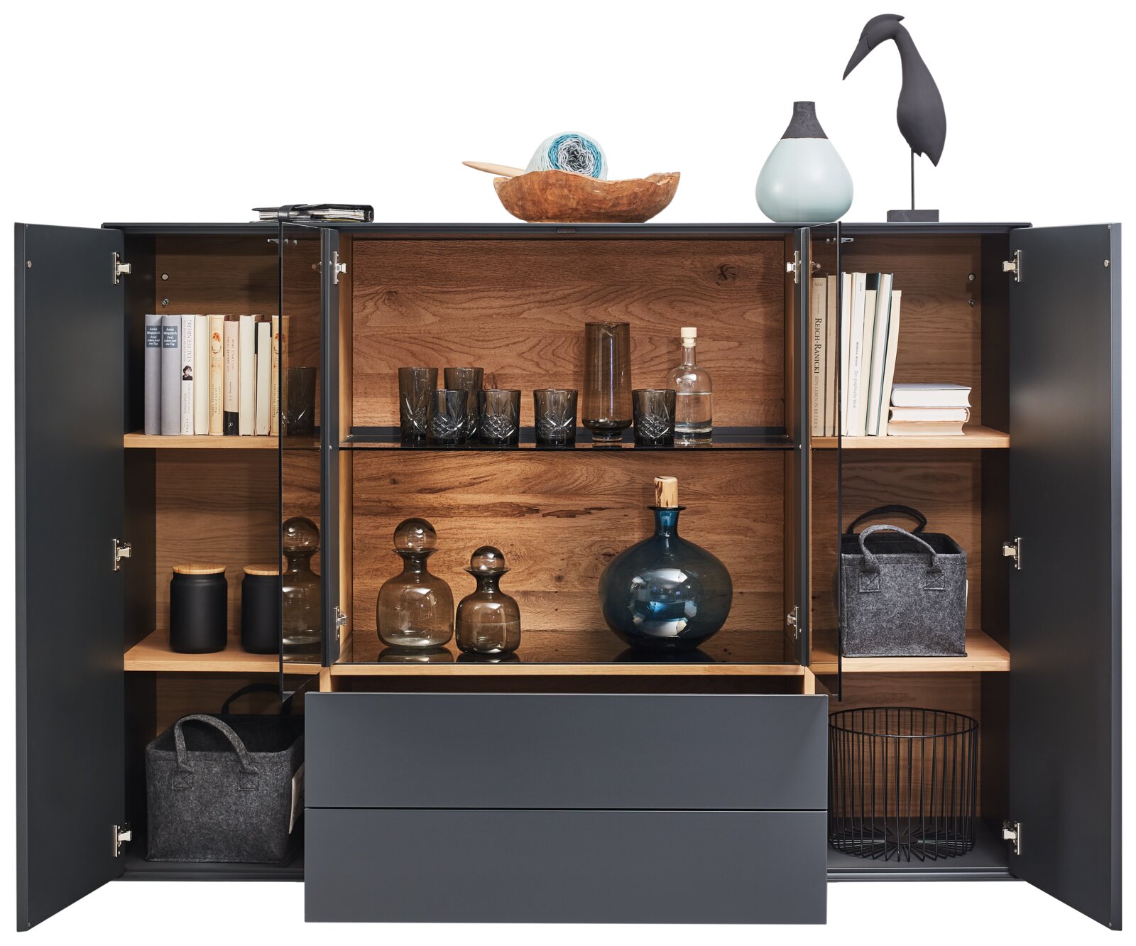 Geöffnetes Highboard mit dunkler Außenfarbe und Holzinneinrichtung, gefüllt mit Büchern, Gläsern und Dekorationsgegenständen, aus frontaler Perspektive.