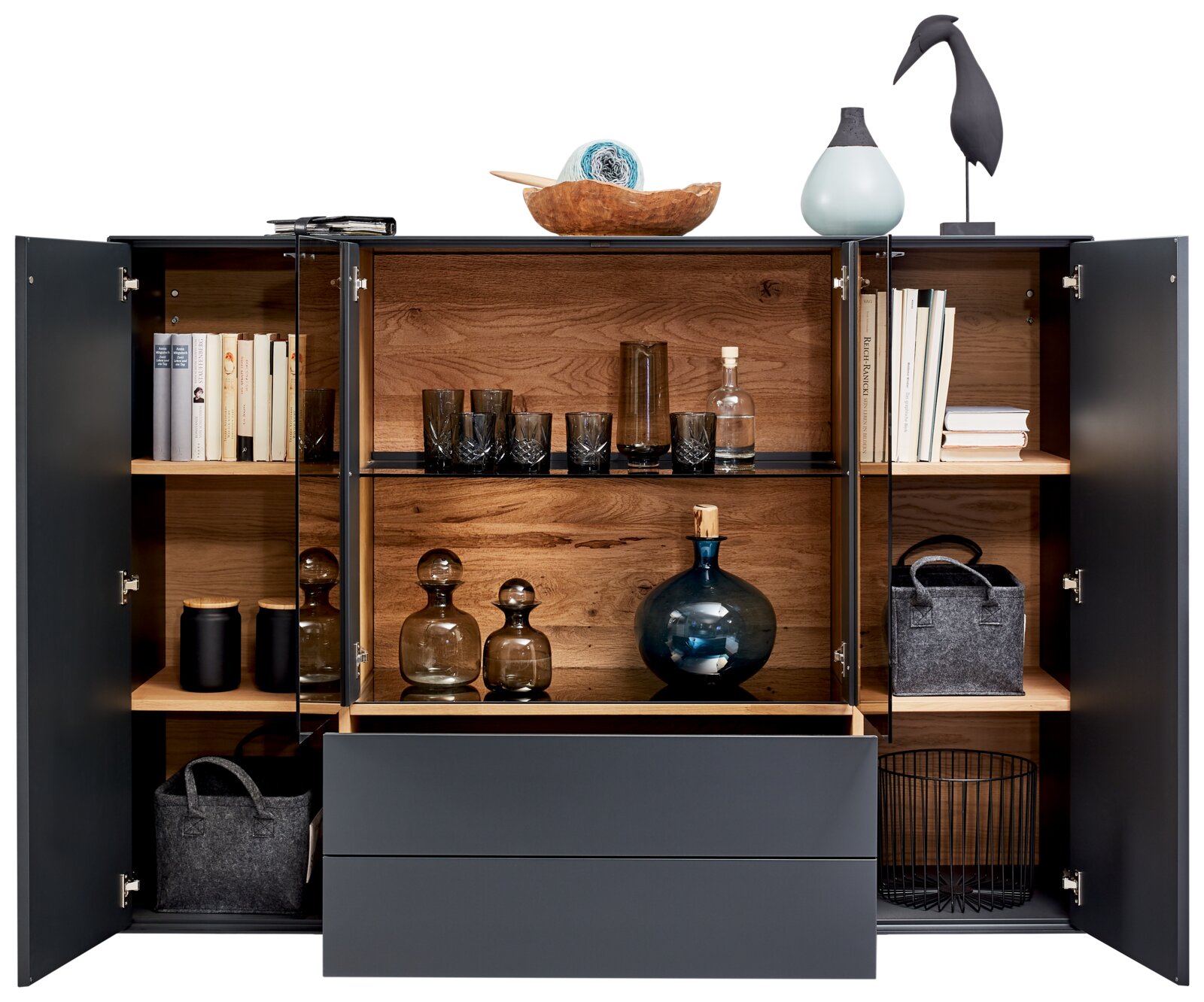 Geöffnetes Highboard mit dunkler Außenfarbe und Holzinneinrichtung, gefüllt mit Büchern, Gläsern und Dekorationsgegenständen, aus frontaler Perspektive.