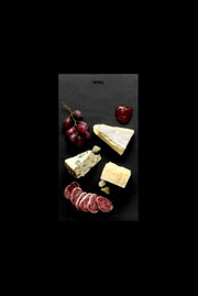 Vogelperspektive auf ein Frühstücksset mit Käse, Wurst, Trauben und Marmelade auf einer schwarzen Platte.