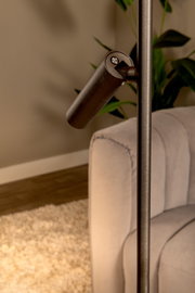 Detailaufnahme aus seitlicher Perspektive: verstellbarer Lampenkopf einer modernen Stehleuchte in dunkler Metalloptik neben einem hellen Sofa im Wohnzimmer