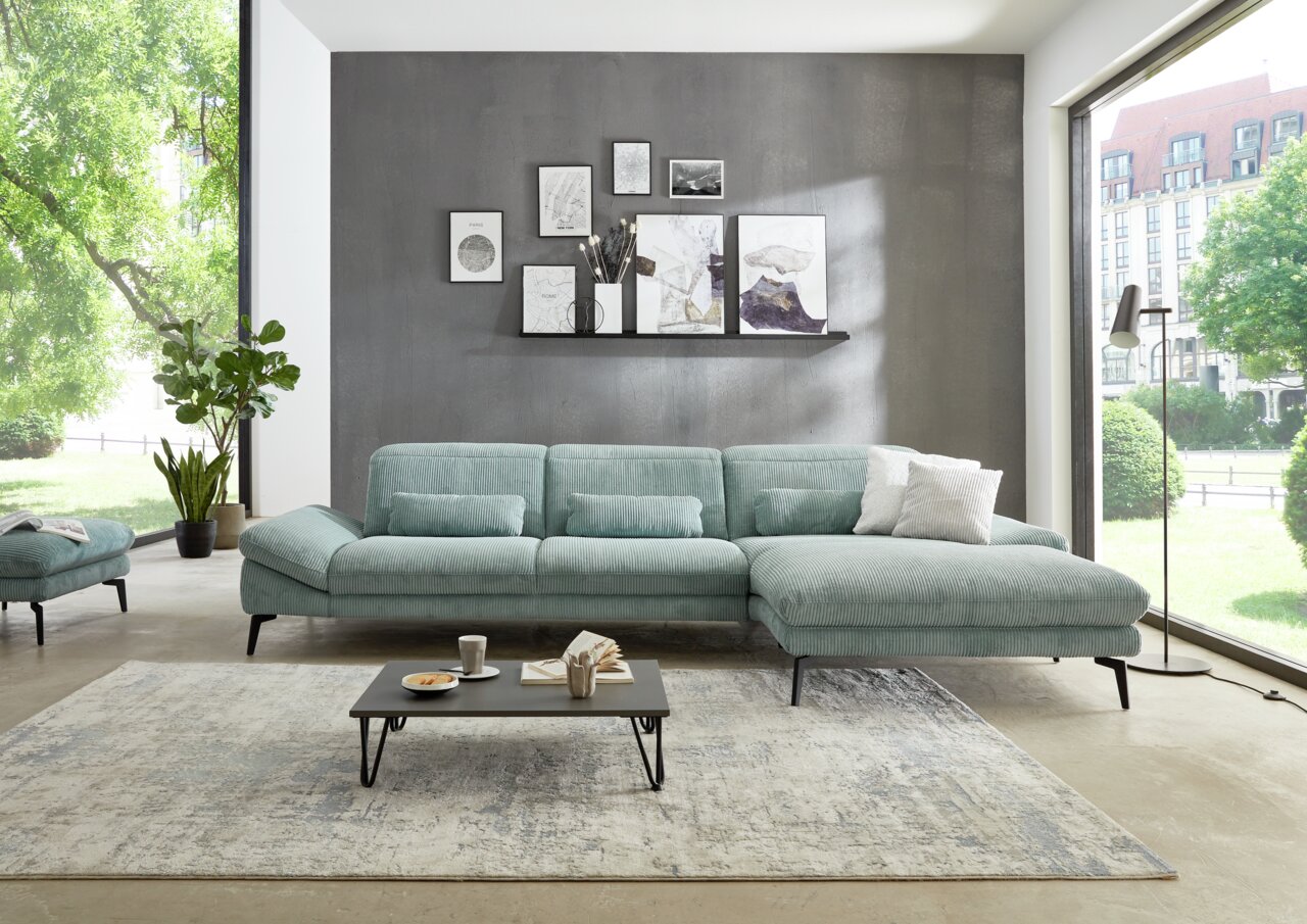 Moderne longchair-combinatie in een lichte woonkamer met grote ramen, een grijze muur en decoratieve schilderijen. Aanzicht van voren.