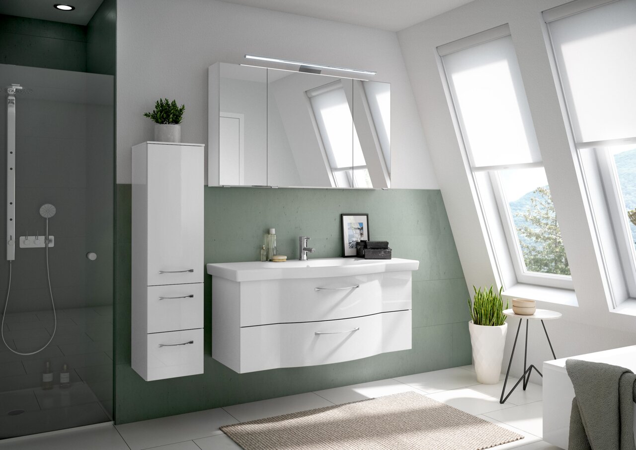 Moderner Badblock in einem hellen Badezimmer mit schrägen Fenstern, bestehend aus einem weißen Waschtisch mit zwei Schubladen und einem hohen Schrank, seitliche Perspektive.