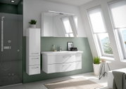 Moderner Badblock in einem hellen Badezimmer mit schrägen Fenstern, bestehend aus einem weißen Waschtisch mit zwei Schubladen und einem hohen Schrank, seitliche Perspektive.