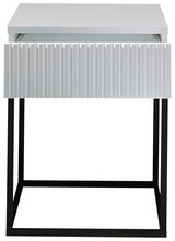 Moderne Nachtkommode mit weißer, geriffelter Front und schwarzem Metallgestell, Frontalansicht.