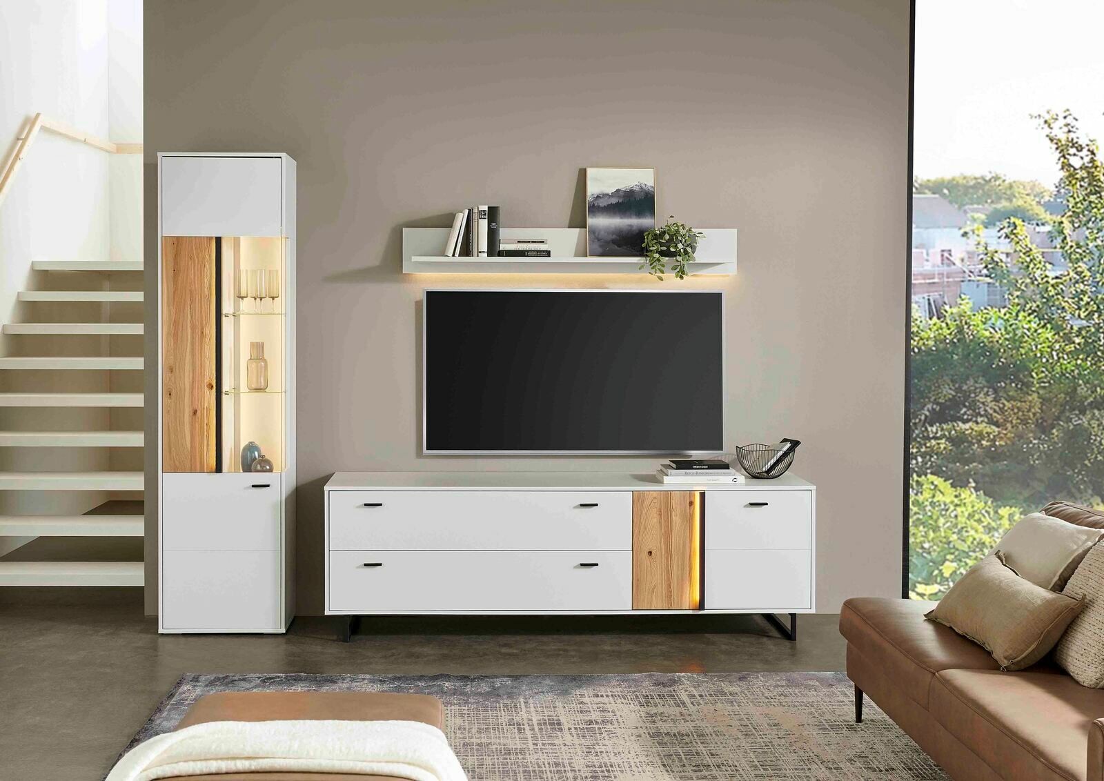 Modernes TV-Lowboard GLASGOW in Weiß mit Holzdetails, frontal abgebildet, neben einem hohen Schrank und unter einem Wandregal.