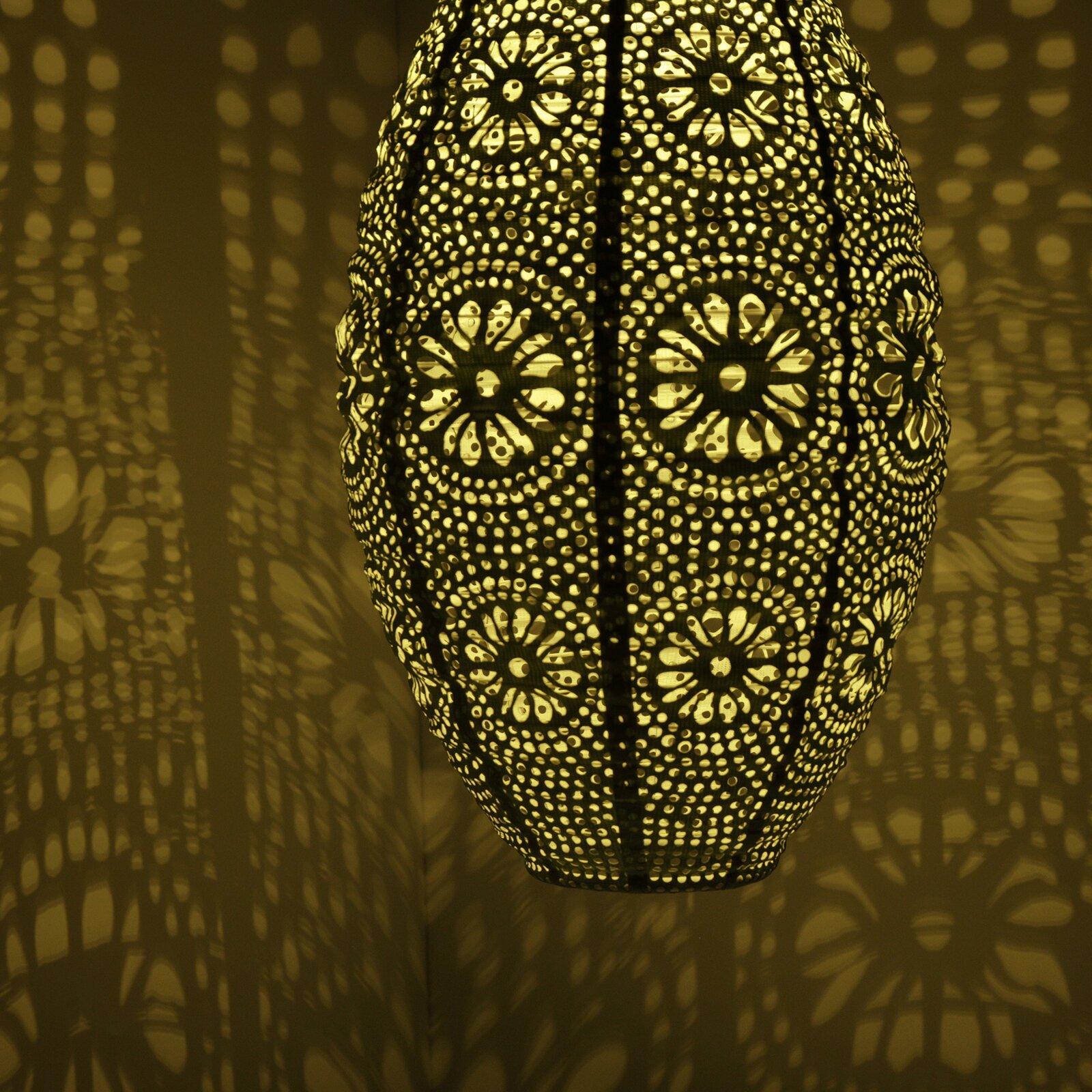 Close-up van een decoratieve zonne-lantaarn met een filigraanpatroon, die een warm licht en fascinerende schaduwen op de muur werpt.