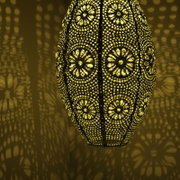 Close-up van een decoratieve zonne-lantaarn met een filigraanpatroon, die een warm licht en fascinerende schaduwen op de muur werpt.