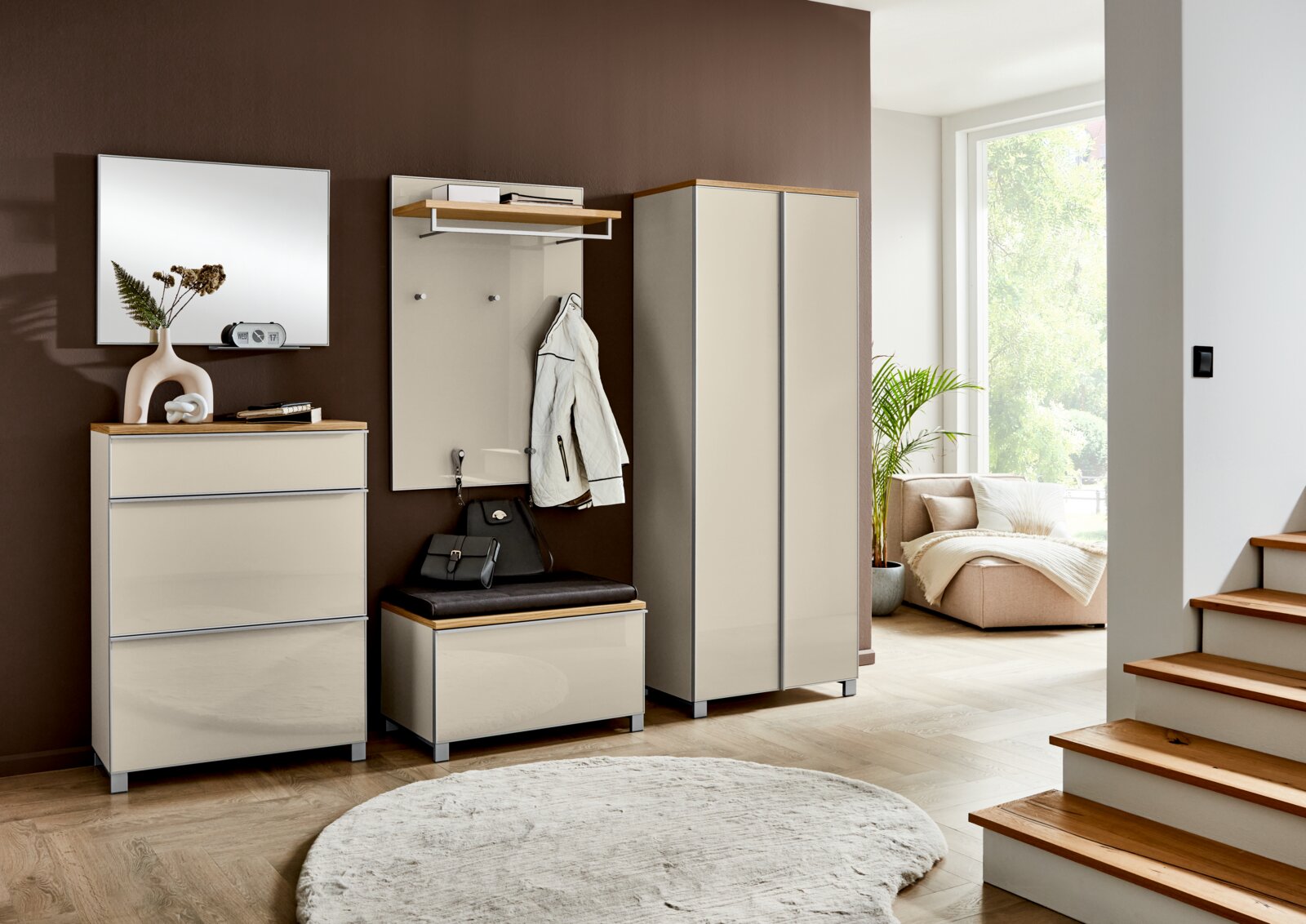 VOSS Garderoben-Set 7-tlg. VORTINA Modernes Garderoben-Set im Flur mit beigem Hochglanz-Schuhschrank, Garderobenpaneel mit Sitzbank und hohem Schrank, Holzablagen und Spiegel an brauner Wand, perspektivisch in leichter Schrägansicht von vorn aufgenommen.