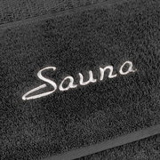 Nahaufnahme eines grauen Saunatuchs mit gesticktem Schriftzug 'Sauna'.