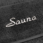 Nahaufnahme eines grauen Saunatuchs mit gesticktem Schriftzug 'Sauna'.