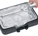 Nahaufnahme eines Tischgrills mit Wasserbehälter, in den Wasser aus einem Glas gegossen wird.