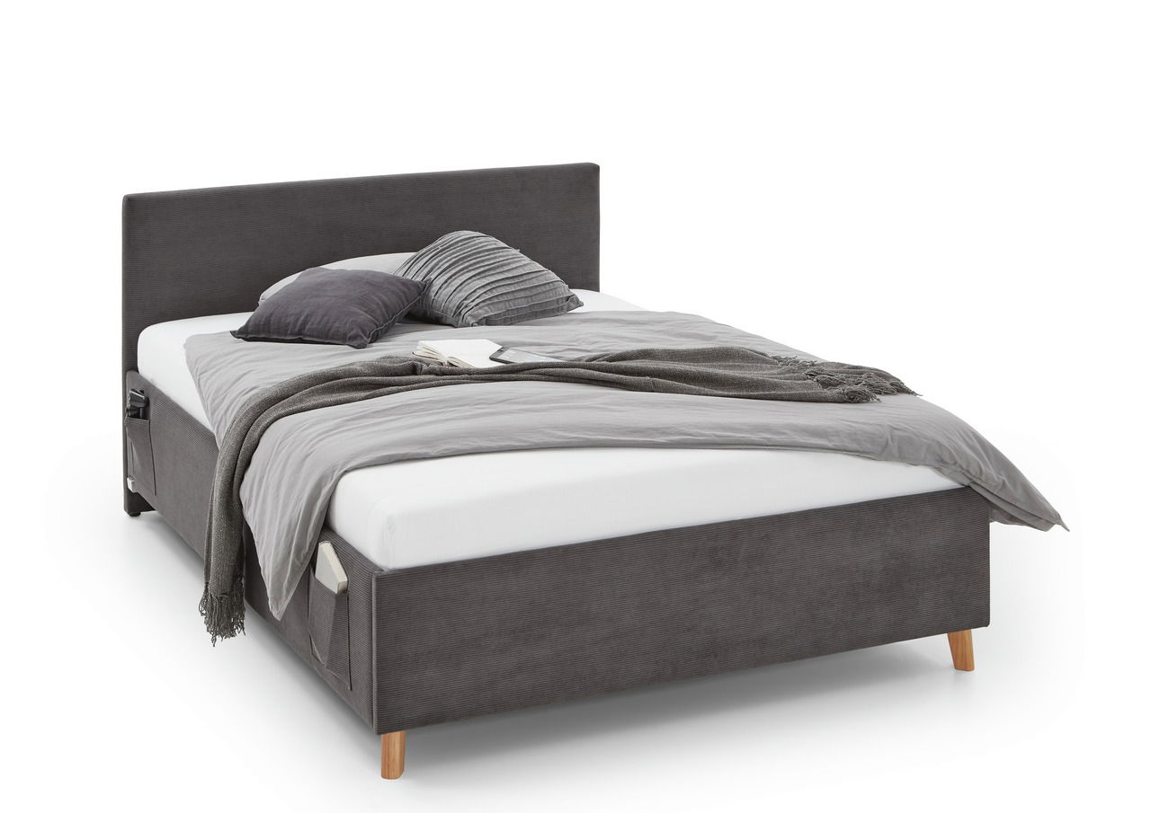 Graue Polsterliege mit Kopfteil, seitlicher Perspektive, dekoriert mit Kissen und Decke.