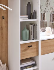 Nahaufnahme einer modernen Kompaktgarderobe mit weißen Regalen und Holzelementen, dekoriert mit Büchern, Vasen und kleinen Deko-Häusern.