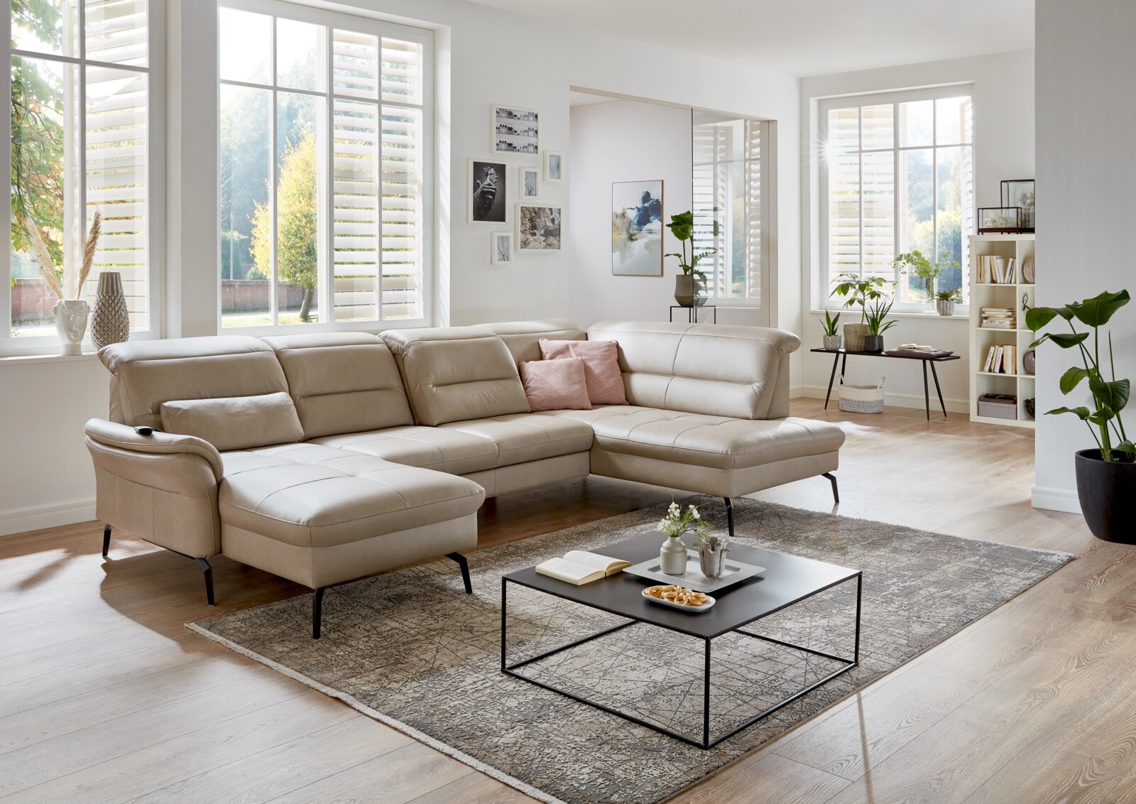 Beige gestoffeerde hoekbank in een moderne woonkamer, gezien vanaf de zijkant, met grote ramen en een stijlvolle inrichting.