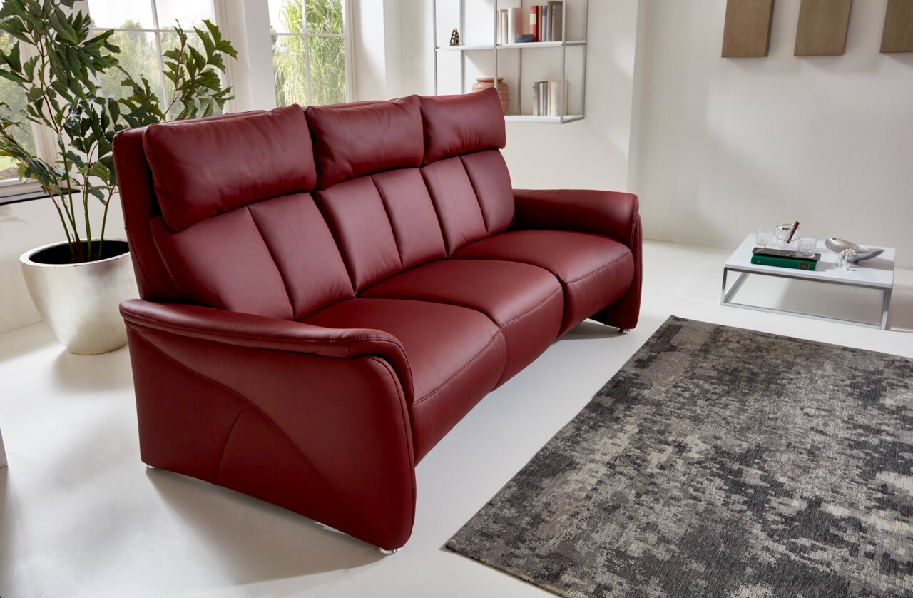Modernes, weinrotes Trapezsofa mit drei Sitzen in einem hellen Wohnzimmer, seitliche Perspektive.