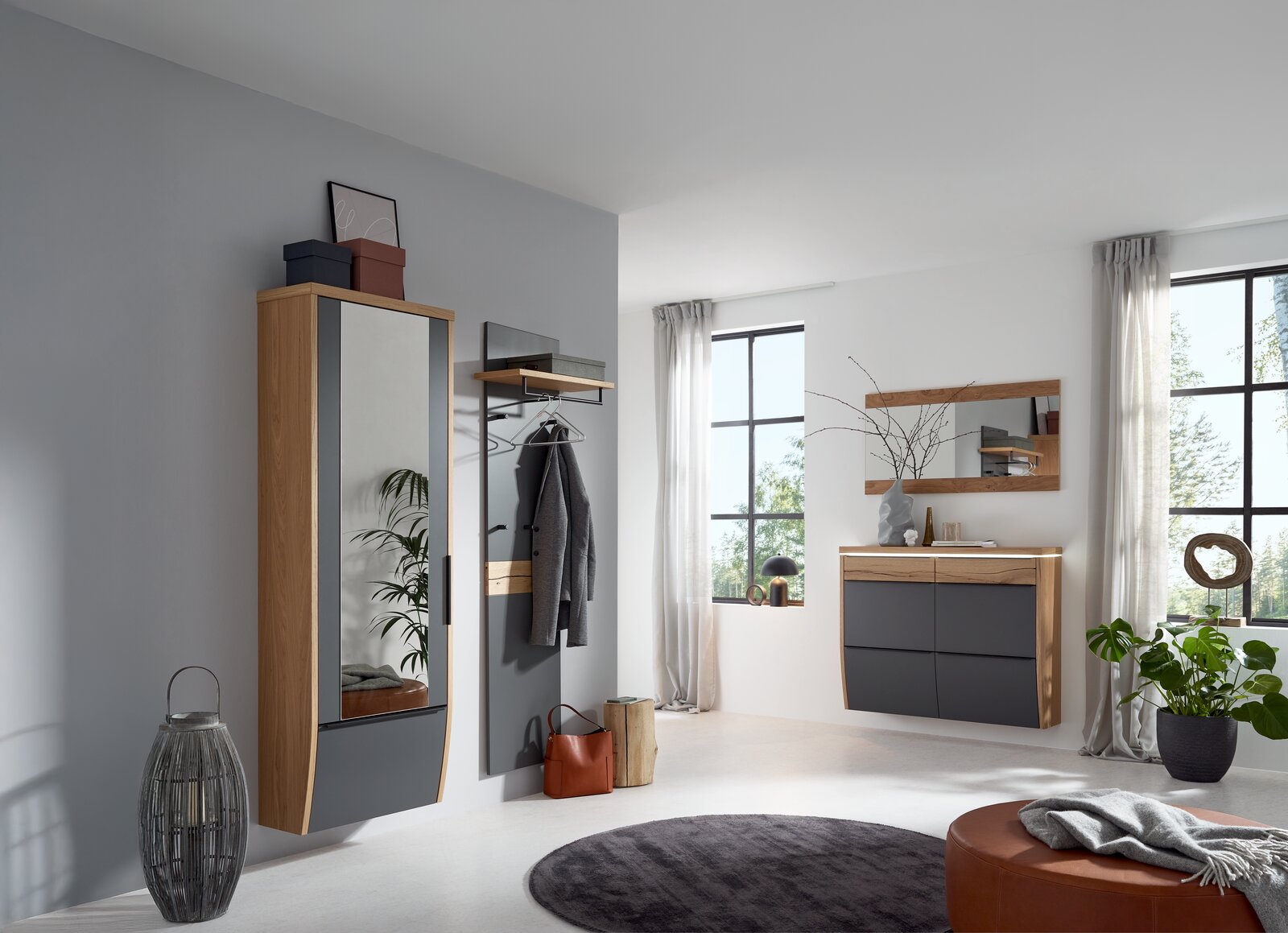 Modernes Flur-Set in Eiche-Optik mit anthrazitfarbenen Fronten: hoher Garderobenschrank mit Spiegeltür, Wandgarderobe mit Ablage und Haken sowie schwebende Kommode mit Spiegel, gezeigt in schräger Frontansicht im hellen Raum.
