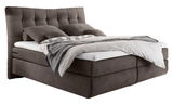 Boxspringbett in seitlicher Perspektive mit gepolstertem Kopfteil und dekorativen Kissen.