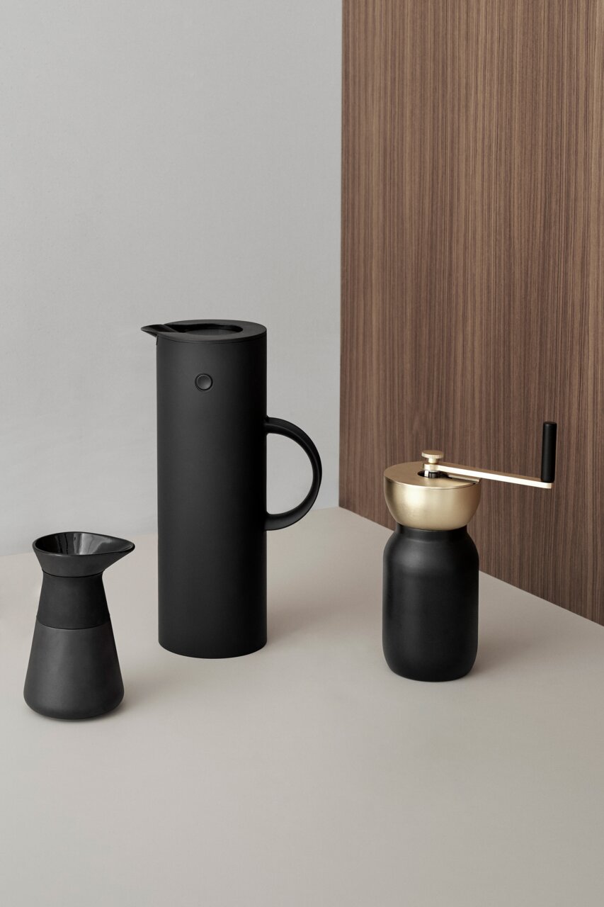 Schwarze Isolierkanne mit 1 Liter Fassungsvermögen, seitliche Perspektive, auf einem Tisch neben einer Kaffeemühle und einem Kaffeefilter.
