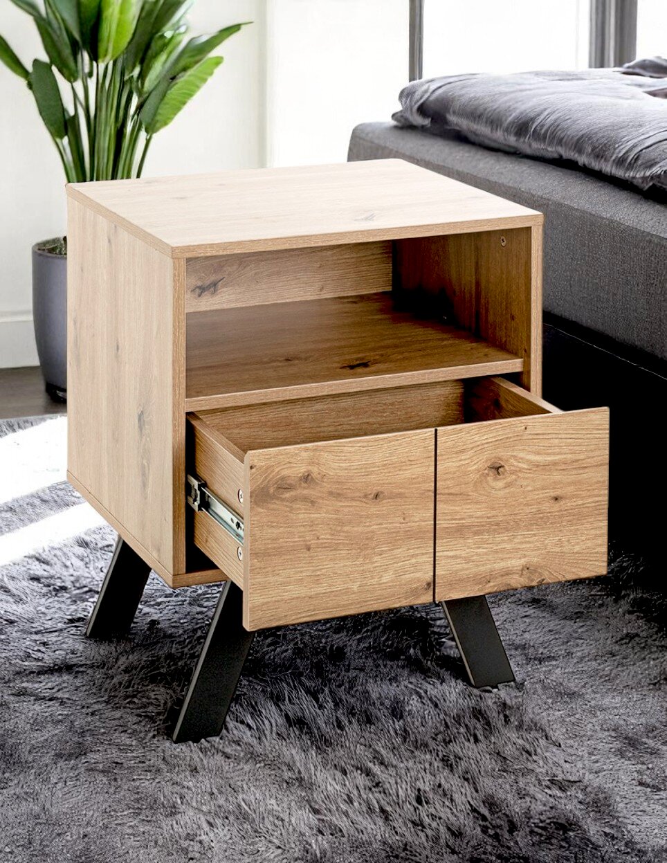 Holz-Nachttisch im modernen Design mit offener Ablage und herausgezogener Schublade auf schwarzen Metallbeinen neben einem Bett, Perspektive: leicht schräg von vorn/seitlich