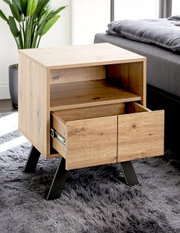 Holz-Nachttisch im modernen Design mit offener Ablage und herausgezogener Schublade auf schwarzen Metallbeinen neben einem Bett, Perspektive: leicht schräg von vorn/seitlich