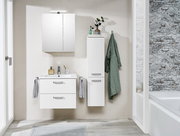 Moderner weißer Midischrank im Badezimmer, frontal fotografiert, neben einem Waschbecken mit Spiegel und Handtüchern.